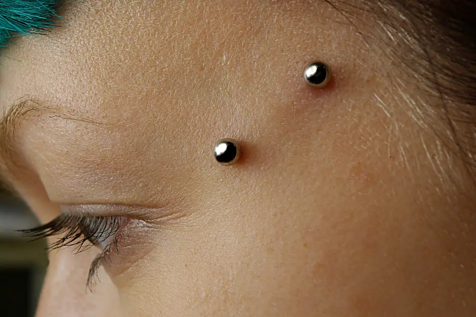 Piercing de superficie en la sien con dos bolitas metálicas visibles