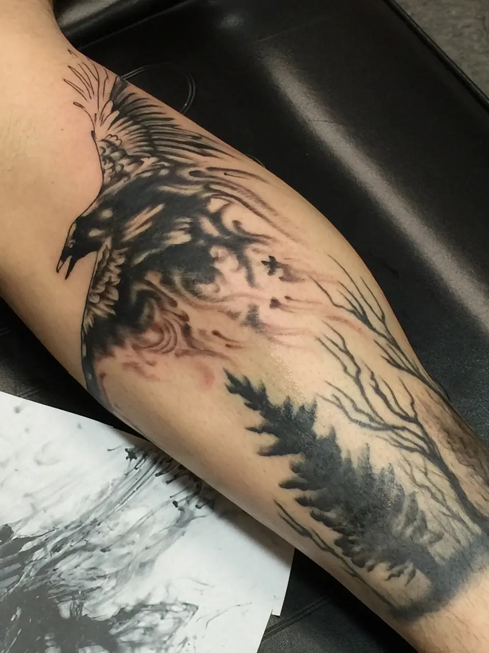 Tatuaje de un cuervo volando sobre un bosque, en el antebrazo