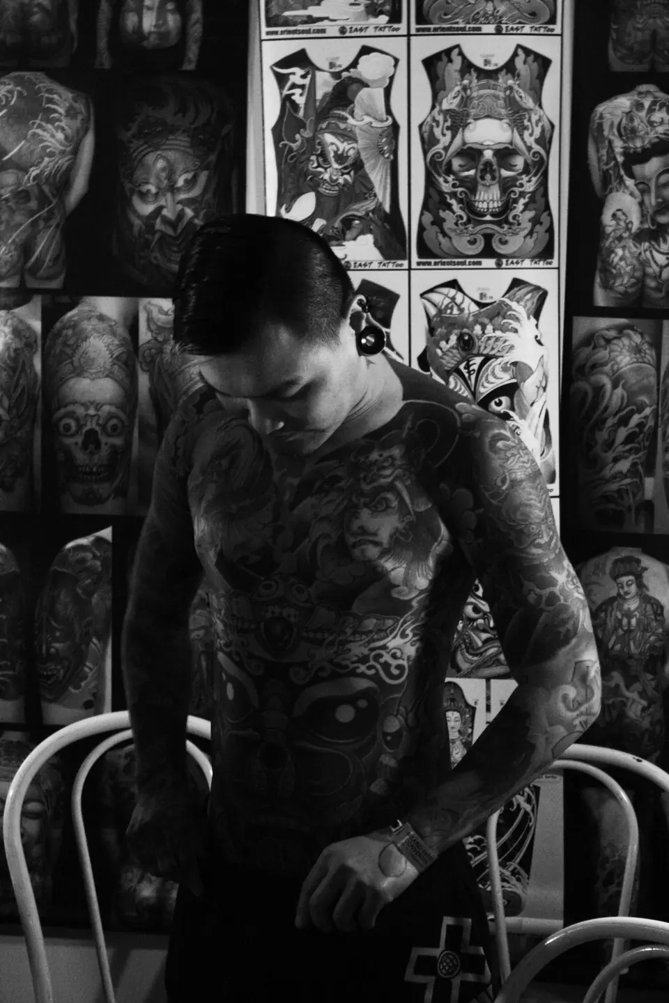 Hombre con tatuaje de espalda completo en un estudio de tatuajes, con diseños en la pared