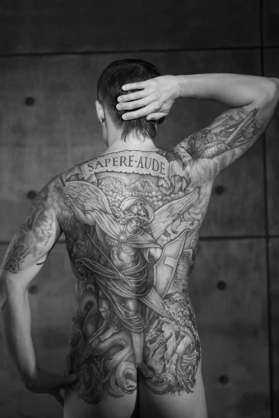 Tatuaje en blanco y negro de un ángel y motivos ornamentales que cubre toda la espalda, con la textura fina de un grabado
