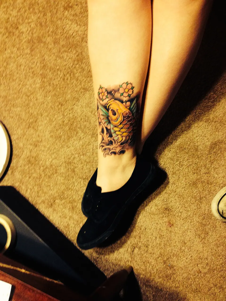 Tatuaje de un pez koi a color en el tobillo, rodeado de flores