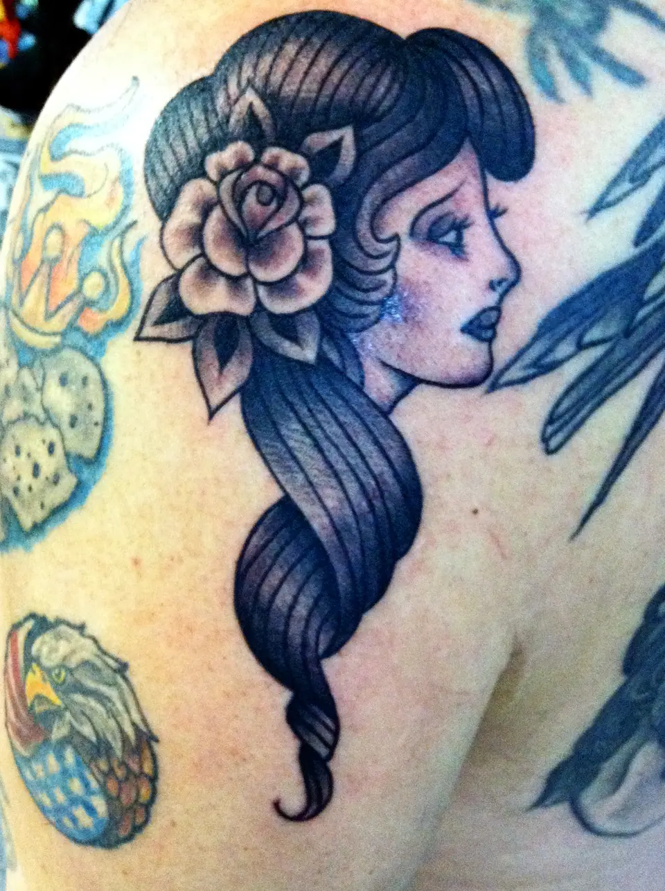 Tatuaje tradicional de rosa junto a un retrato de mujer en el hombro